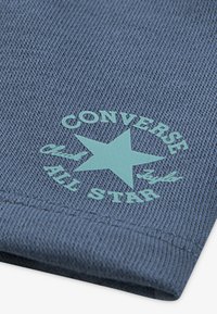 Modrý textil s tkanou strukturou; tištěný mátově zelený text "Converse Chuck Taylor All Star" a hvězdné logo v dolním rohu.