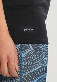 Primo piano di una mano appoggiata accanto a leggings azzurri a motivo e l'orlo di una maglietta sportiva DRI-FIT nera.