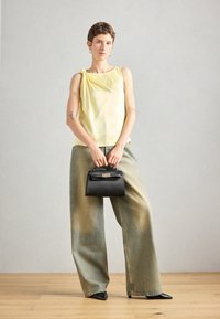 Gul satin tanktop med sidesløjfe-detalje, parret med løse, falmede grønne denimbukser. Sort struktureret håndtaske og spidse sorte sko.