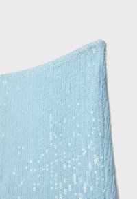 Coin de tissu bleu clair couvert de petites paillettes brillantes créant une surface texturée et réfléchissante sur un fond uni.