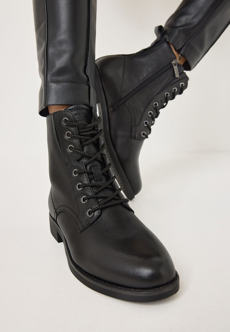 Botas de cuero negro hasta el tobillo con punta redonda, cordones en la parte delantera y cremallera lateral. Acabado texturizado y suela de goma resistente.