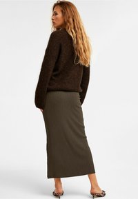 Brun strukturerad tröja i kombination med en lång, ribbad mörkgrön kjol. Modellen bär klackar med djurmönster, vilket visar upp en avslappnad outfit.