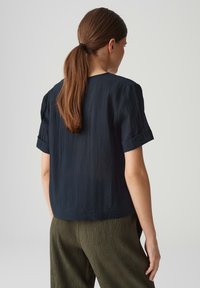 Maglietta blu navy a maniche corte con finitura texture e risvolti, abbinata a pantaloni a palazzo pieghettati verde oliva.