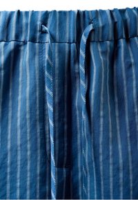 Blå bukser i stof med hvide lodrette striber og elastik i taljen med snøre foran i midten.