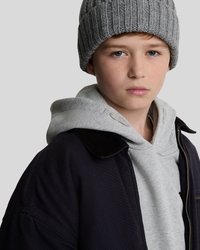 Cappello a coste grigio, felpa grigia e giacca nera con colletto in velluto. Vista ravvicinata focalizzata su viso e parte superiore del corpo, sfondo neutro.
