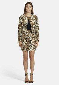 Veste courte en imprimé léopard avec un col rond, assortie à une mini jupe. Haut noir en dessous et escarpins noirs à brides.