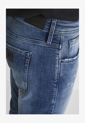 Jeans in denim blu con vestibilità slim, caratterizzati da una finitura texturizzata, un'etichetta in pelle nera in vita e tasche posteriori a toppa.