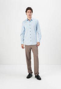 Light blue long-sleeve shirt with a pointed collar and dark buttons, paired with beige trousers and black shoes, set against a white background.