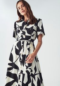 Šaty na gombíky v čiernej a bielej farbe s listovým vzorom. Krátke rukávy, úzky pás a priehľadné gombíky po celej dĺžke vpredu. Textúrovaná látka.