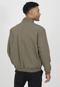 Oliwkowa bomberka z kołnierzem stójkowym, elastycznymi mankietami i ściągaczem w pasie. Charakteryzuje się gładką, matową fakturą oraz prostym wzornictwem.