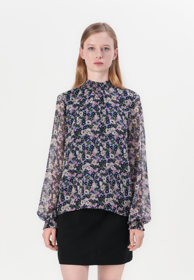 Blusa floreale trasparente con colletto alto arricciato, maniche lunghe con polsini elasticizzati e tessuto scuro a fantasia con fiori rosa e crema.