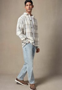 Kariertes Flanellhemd in hellbeige mit braunen Akzenten, kombiniert mit hellblauen Jeans und braunen Sneakers. Schlichte, lässige Passform.