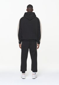 Sudadera negra con pantalones de chándal que tienen paneles laterales beige. Tejido suave, corte holgado y puños acanalados. Combinado con zapatillas deportivas blancas.