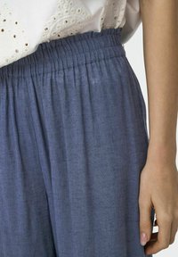 Pantalons en lin bleus avec une taille élastique, présentant une texture douce et des plis lâches, associés à un haut léger brodé.