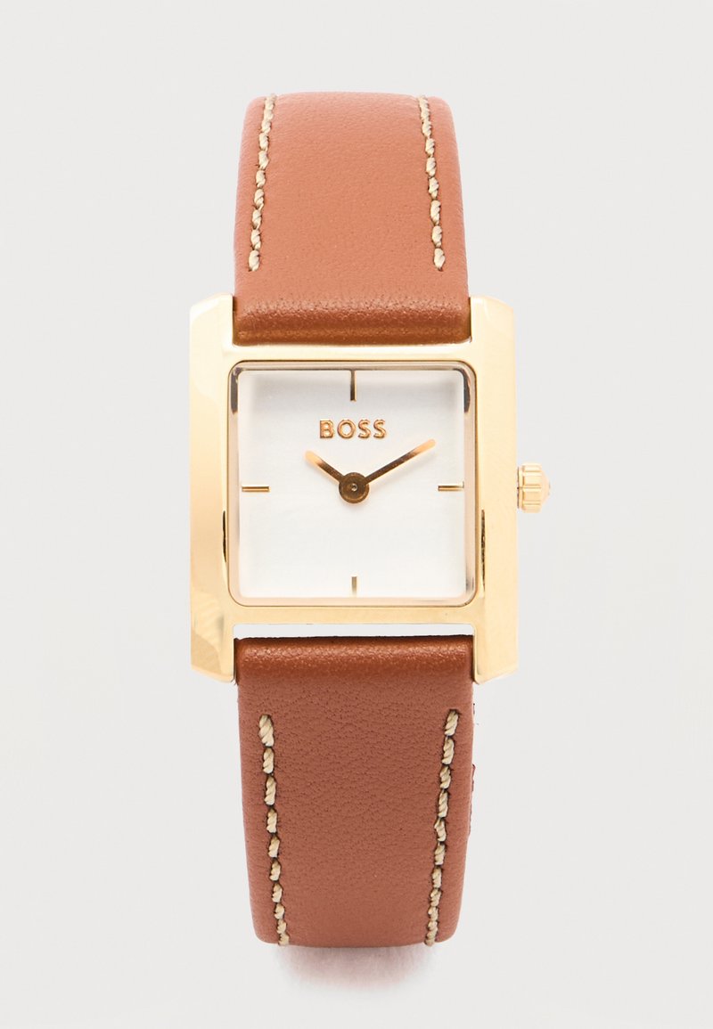 Τετράγωνο χρυσό ρολόι με λευκό καντράν, καφέ δερμάτινο λουράκι με λευκή ραφή και χρυστά δείκτες ώρας και λεπτών που δείχνουν 10:10.