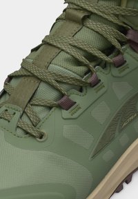 Κοντινό πλάνο πράσινου πεζοπορικού παπουτσιού με κορδόνια με σχέδιο, υφασμάτινο πλέγμα, ενισχυμένες τρύπες και υφασμένη σόλα με την επωνυμία «Altra».