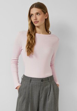 Jasnoróżowa bluzka z długim rękawem wykonana z miękkiego materiału, z okrągłym dekoltem, zestawiona z szarymi spodniami w prążki o bocznych kieszeniach.
