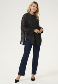 Melna, caurspīdīga adīta blūze ar brīvu piegriezumu, garām piedurknēm un smalku spīdumu. Kombinēta ar ziliem taisnajiem džinsiem un melniem stūrīšu zābakiem.