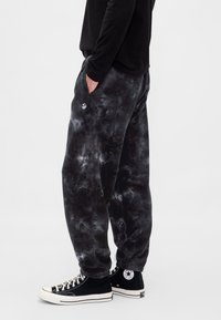 Spodnie dresowe w czarno-szary wzór tie-dye, z bocznymi kieszeniami, elastycznymi mankietami i naszywką z logo na lewym biodrze.