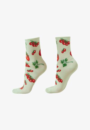 Helle Cremesocken mit Muster aus roten Kirschtomaten und grünen, blättrigen Stielen, gezeigt an Füßen in stehender Position.