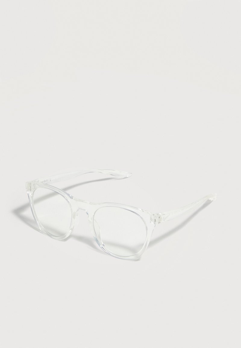 Montures de lunettes carrées transparentes et claires avec des bords légèrement arrondis et des charnières visibles reposant sur une surface claire et unie.