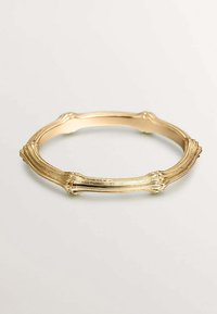 Pulsera de oro en forma de brazalete con una superficie texturizada y ondulada, y acanaladuras distintas. Acabado interior suave, forma circular y brillo metálico.