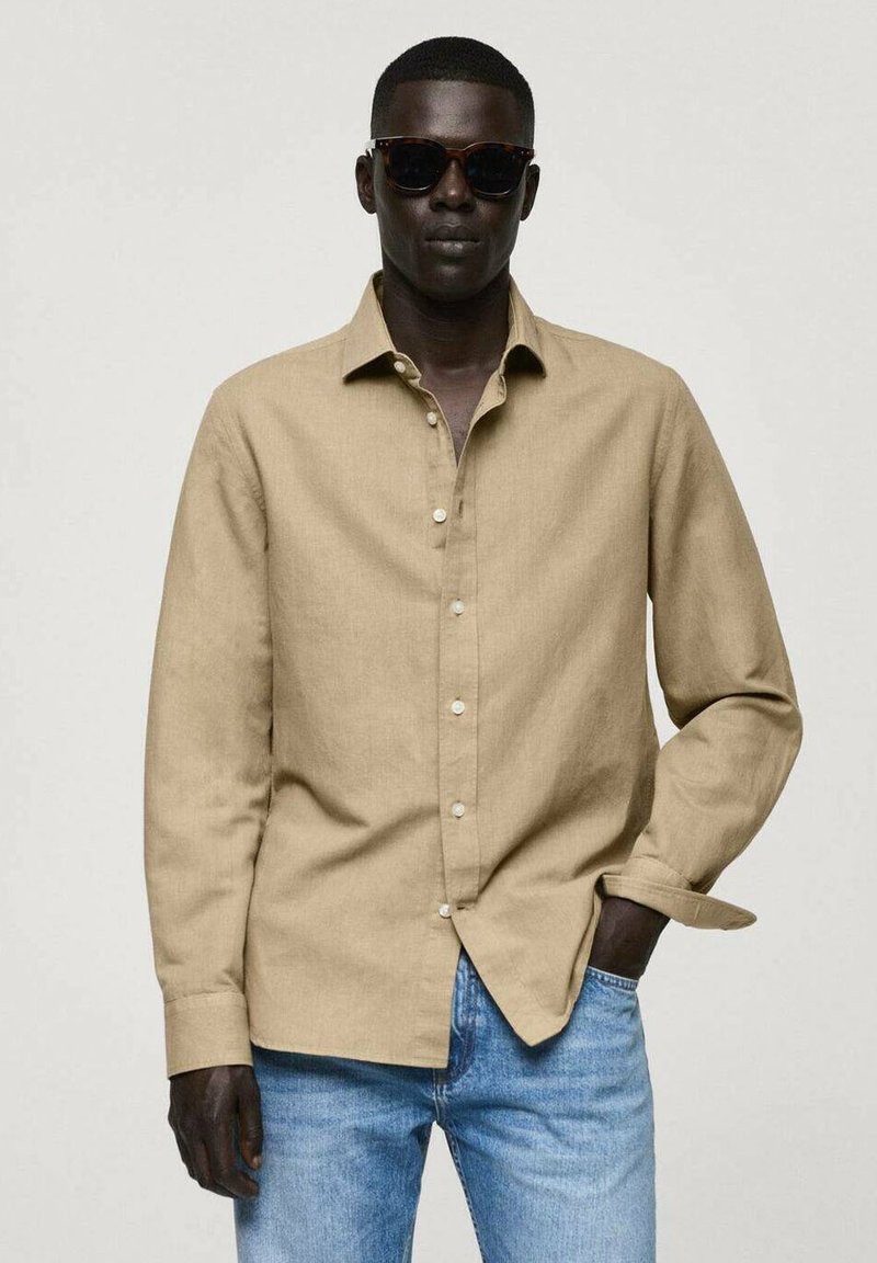 Beige linned skjorte med spids krave, lange ærmer og knaplukning foran. Sammen med lyseblå jeans skaber det et afslappet look.