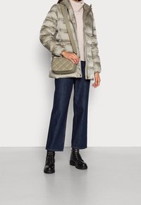 Giacca beige voluminosa, maglione leggero lavorato a maglia, pantaloni a gamba larga in denim scuro e stivaletti neri con lacci. L'outfit include una borsa a tracolla con design trapuntato.