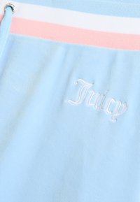 Gaiši zils audums ar mīkstu tekstūru, kam ir balta un rozā svītru josta un balts izšūts "Juicy" logotips.