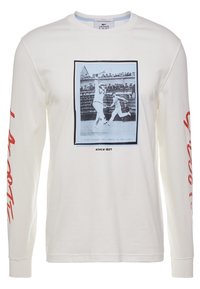 T-shirt bianco a maniche lunghe con una grafica blu di due giocatori di tennis, testo rosso sulle maniche e design a girocollo. Materiale in cotone morbido.