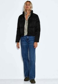 Casaco puffer preto cropped com gola alta, usado sobre um suéter cinza, combinado com jeans de perna larga azuis e sandálias verde-escuras.