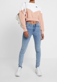 Avkortad sweatshirt med färgblock i vitt och persika, rund halsringning, och parat med ljusblå skinny jeans och vita sneakers.