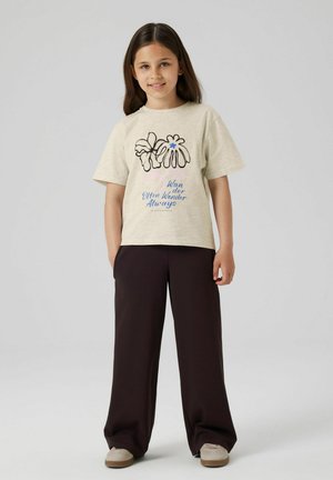 Beige T-Shirt mit kurzen Ärmeln, floralem Grafikdesign und Text. Kombiniert mit dunkelbrownweit geschnittenen Hosen und beigen Sneakern. Glatte Stofftextur.
