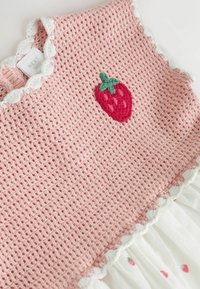 Haut en tricot rose avec un bord en tissu blanc à festons, orné d'un motif de fraise brodé. Le bas comprend une couche de tissu blanc imprimée de petites fraises.
