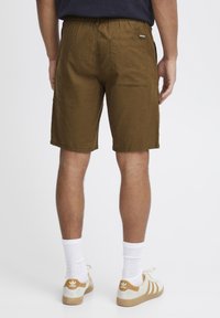 Brune, mellemlange shorts med elastisk talje, baglomme og en glat overflade; parret med hvide sokker og cremede sneakers.