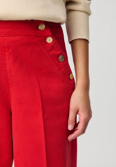 Pantalones de mezclilla de pierna ancha en rojo, con grandes botones dorados de un lado y una textura suave, con un diseño de cintura alta.