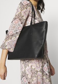 Borsa tote in pelle nera con una texture liscia, apertura superiore e due manici robusti. Design semplice senza hardware o decorazioni visibili.