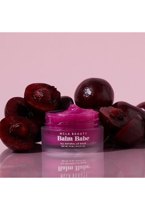 Pink lip balm in a clear, round container with a twist-off lid, surrounded by dark red cherries on a light pink background.