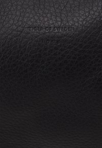 Svart läderplånbok med en strukturerad yta. Har en präglad logotyp "TIGER OF SWEDEN" och året "1903." Enkel, elegant design.