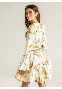 Vestido floral con mangas largas y acampanadas, fondo marfil y flores en tonos pastel. Presenta una cintura ajustada y una falda amplia y acampanada.
