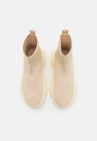 Bottines en tricot beige à la cheville avec un design côtelé, texture douce, languette à l'arrière et semelle en caoutchouc épaisse de couleur jaune clair.