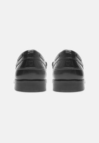 Zwarte lederen schoenen met een gepolijste afwerking, ronde neus, platte hak en subtiele stiksels. De achterkant toont een gladde textuur.