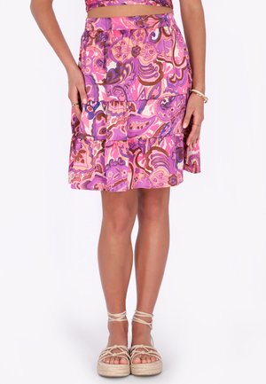 Donna che indossa una gonna a balze con motivo floreale rosa e viola abbinata a sandali beige con plateau e cinturini alla caviglia.