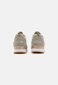 Šedé semišové a síťované sportovní boty s gumovou podrážkou, které mají polstrovanou patu, poutko na patě a vyražené logo značky na zadní straně.