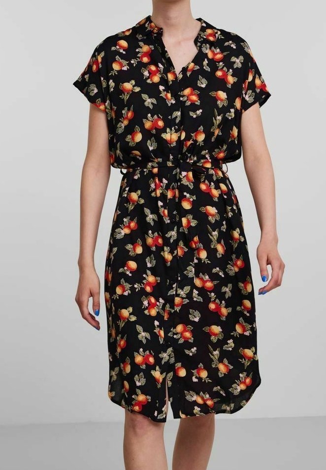 Personne portant une robe noire à manches courtes avec un col, des boutons devant, une ceinture à la taille et un motif de fruits rouge-orangé et de feuilles.