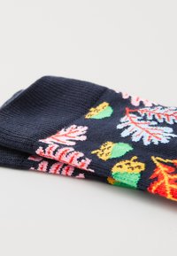 Chaussettes bleu foncé pliées avec des feuilles d'automne colorées et des glands verts en motif sur le tissu, sur une surface blanche.