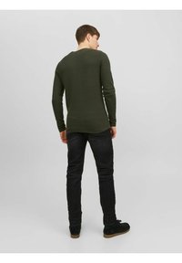 Oliven grøn, struktureret langærmet skjorte med rund halsudskæring, parret med sorte jeans og mørke sko, set bagfra.