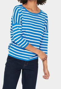 Modrý a bílý pruhovaný top s tříčtvrtečními rukávy, kulatým výstřihem a volným střihem, doplněný tmavě modrými džínami.