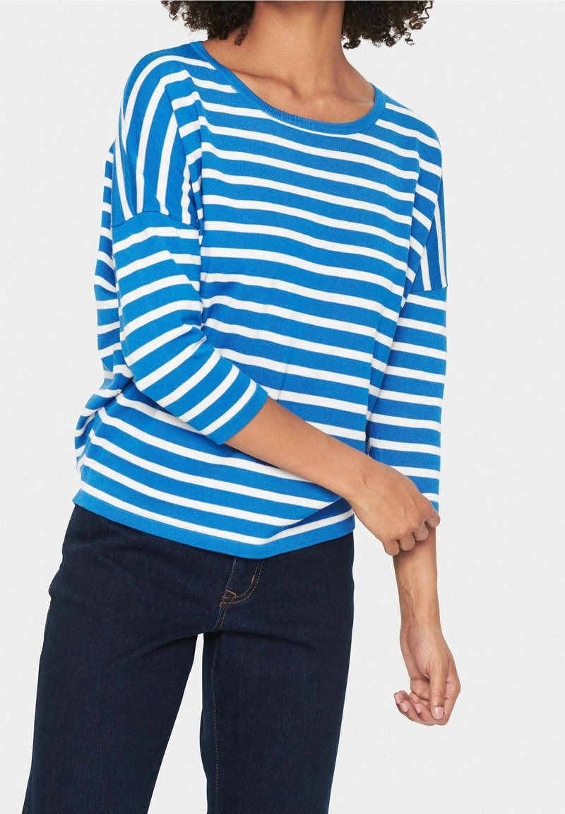 Modrý a bílý pruhovaný top s tříčtvrtečními rukávy, kulatým výstřihem a volným střihem, doplněný tmavě modrými džínami.