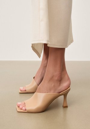 Jalad, mis kannavad beežikaid avatud varbakandaga kontsakingi ruudukujulise varba ja lehvikukujulise kontsaga, koos kreemja sirge lõikega pükstega.